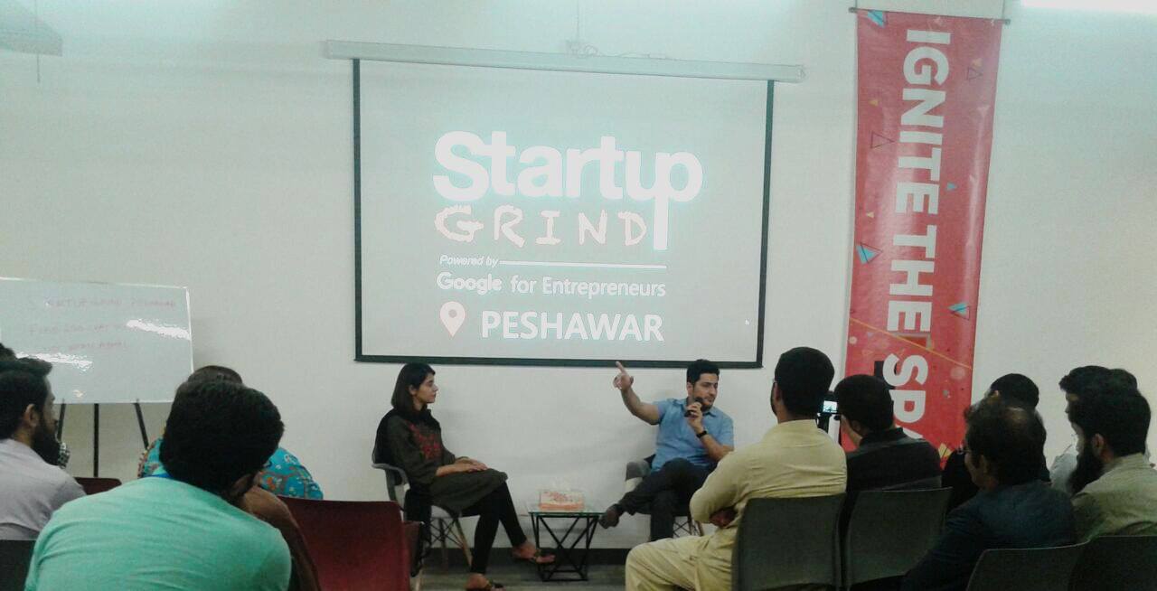 Syed Irfan Ajmal in a fireside chat with a microphone, in front of a Startup Grind Powered by Google for Entrepreneurs screen in Peshawar